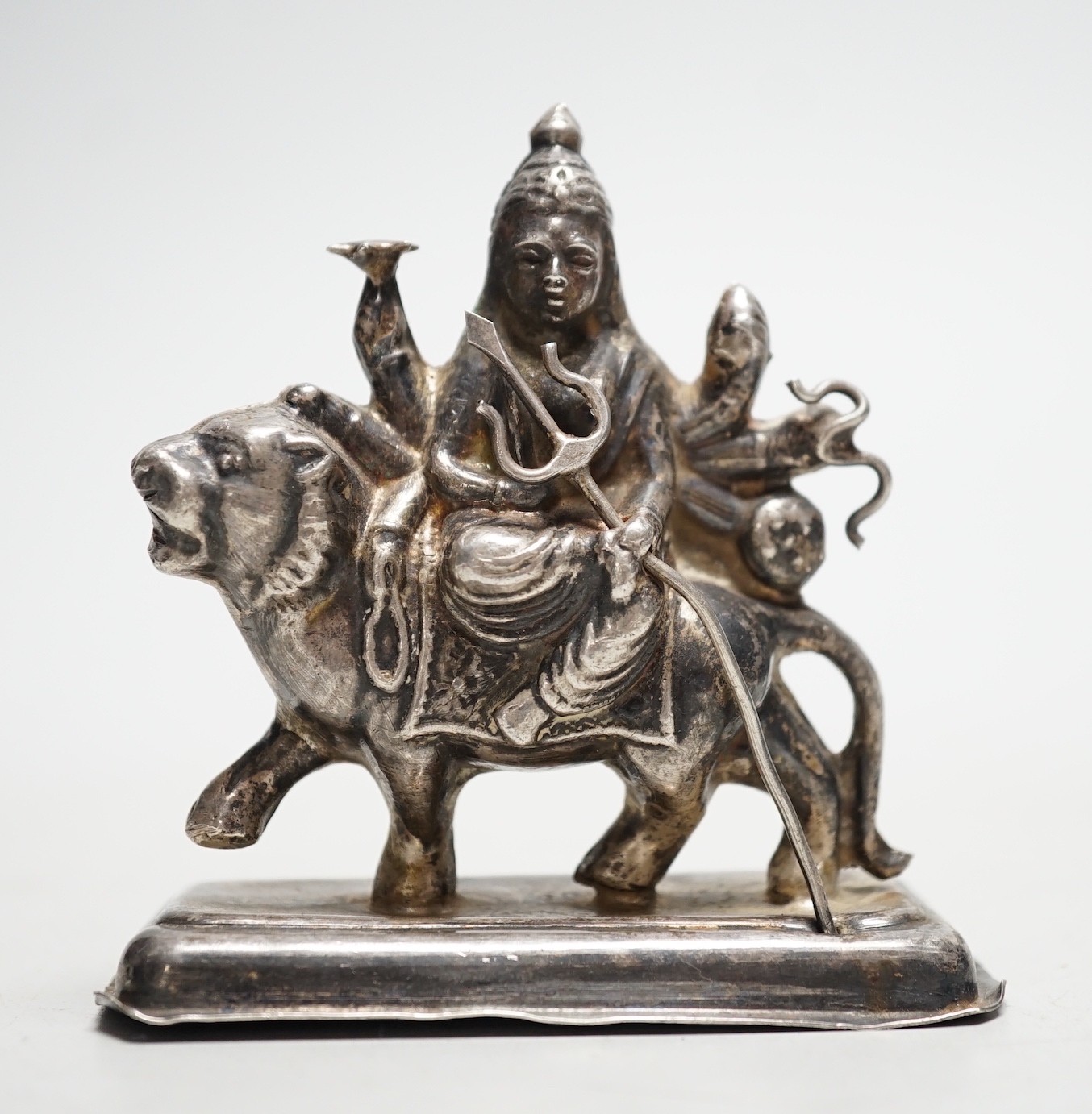A Buddhist white metal group of a Bodhisattva riding a lion, 8cm tall